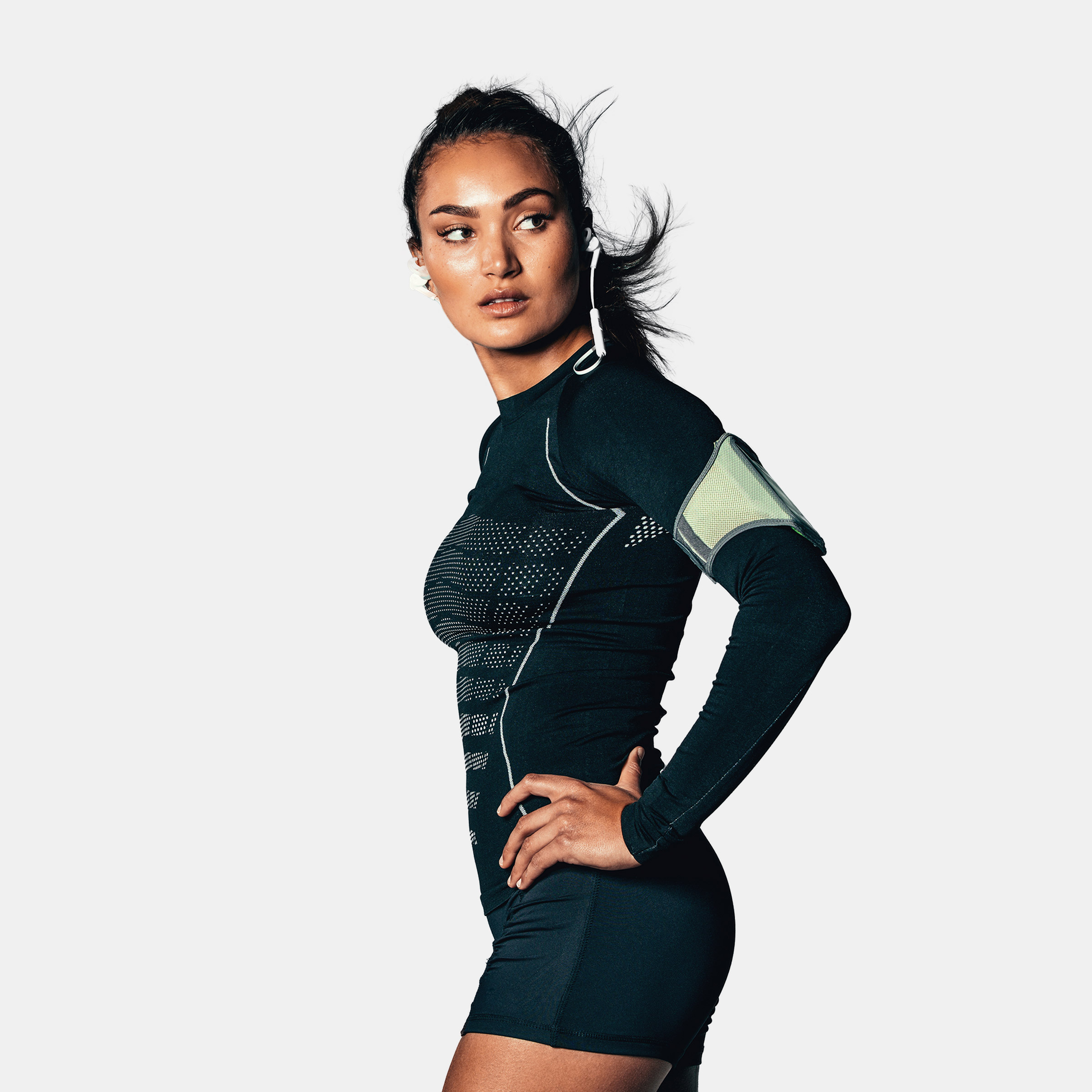 Athletic woman wearing headphones, looking over her shoulder, hands on her hips