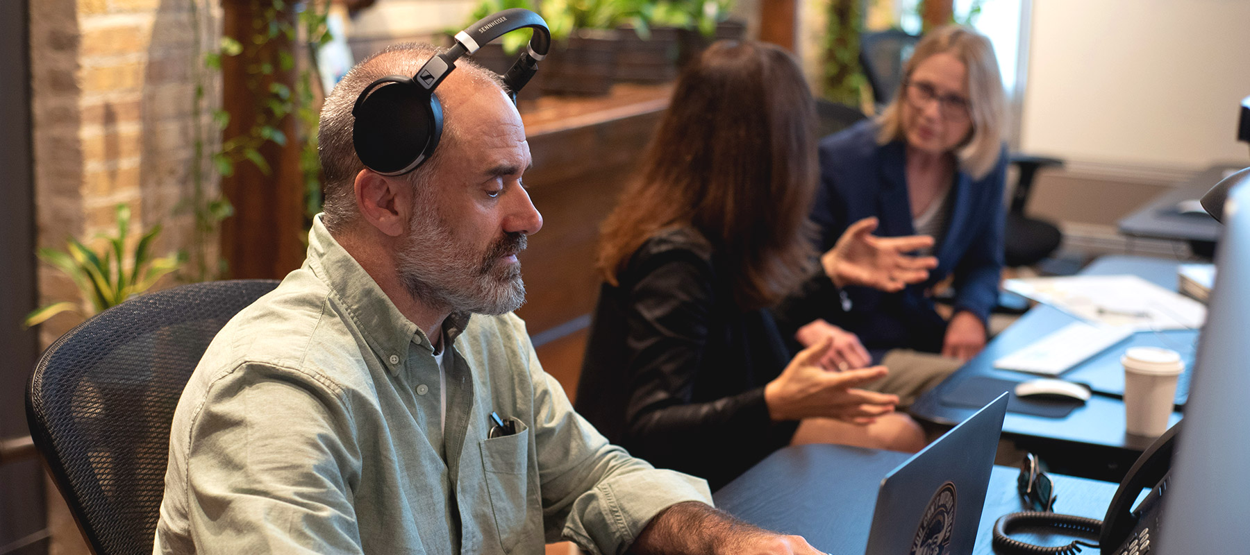 service-page-image-content-development man with headphones on working in office, women talking in background