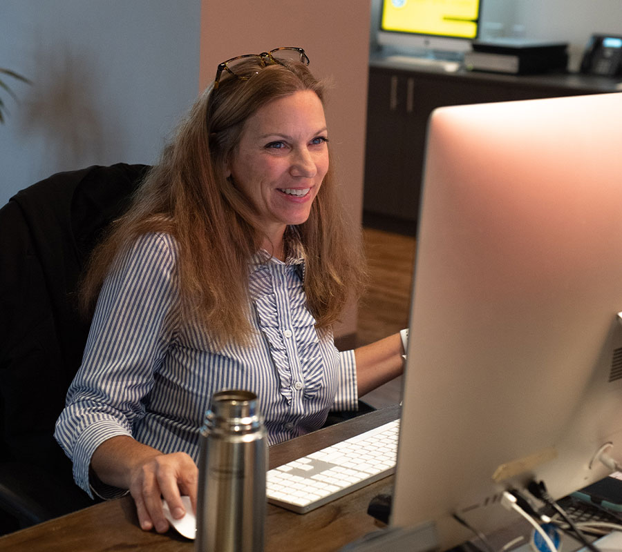 staff-amy-1122-01 woman smiling at desk